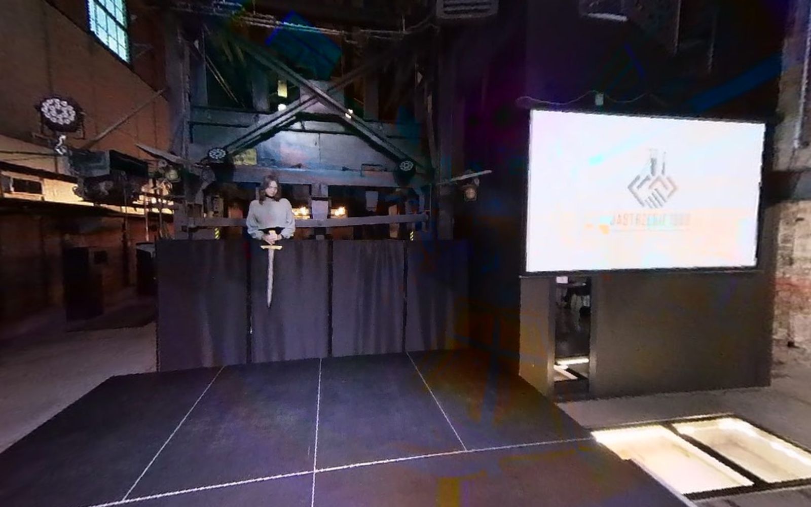 Kadr z filmu 360°: podest sceny z ciemną kotarą, po lewej ekran z projekcją, przed sceną podświetlone szyby w podłodze.